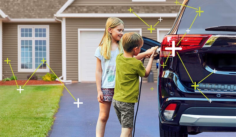 Two children (boy and girl) charging an EV parked in the driveway of their home
