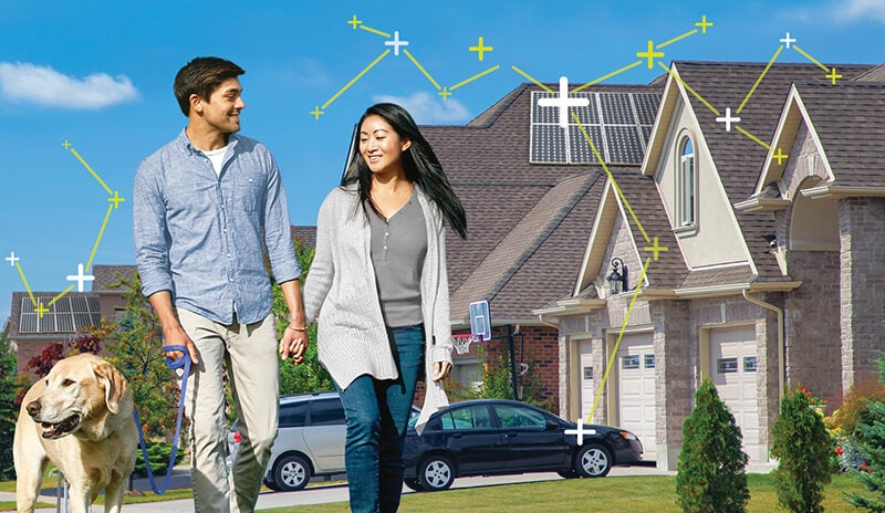 Man and a woman walking their dog in front of a house with Solar panels on its roof